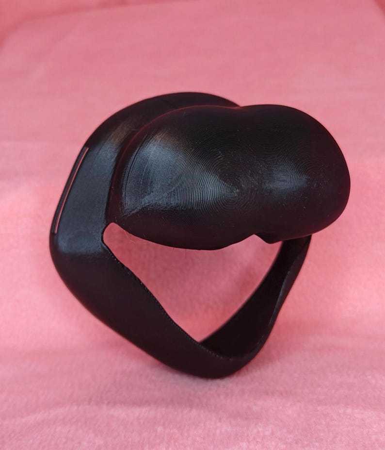 May include: A black 3D printed face mask with a curved design. The mask has a large opening for the nose and mouth.