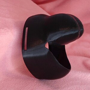 May include: A black 3D printed object with a curved shape and a small rectangular opening. The object is made of a smooth, matte material.