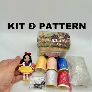 Peut inclure: Un kit de crochet pour réaliser une poupée Blanche-Neige. Le kit comprend du fil de différentes couleurs, une petite boîte en étain au design vintage et un patron. La poupée porte une robe jaune avec un nœud rouge.