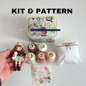 Peut inclure: Un kit de poupée au crochet avec de la laine, un crochet, du rembourrage et une carte de remerciement. La poupée porte une veste marron, une robe verte et des bottes marron. La poupée tient un animal en crochet blanc.