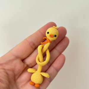 May include: A handmade yellow crochet duck with orange accents. The duck has a knotted neck, small wings, and orange feet. It is a whimsical, handcrafted item, perfect for a child's toy or a decorative piece.