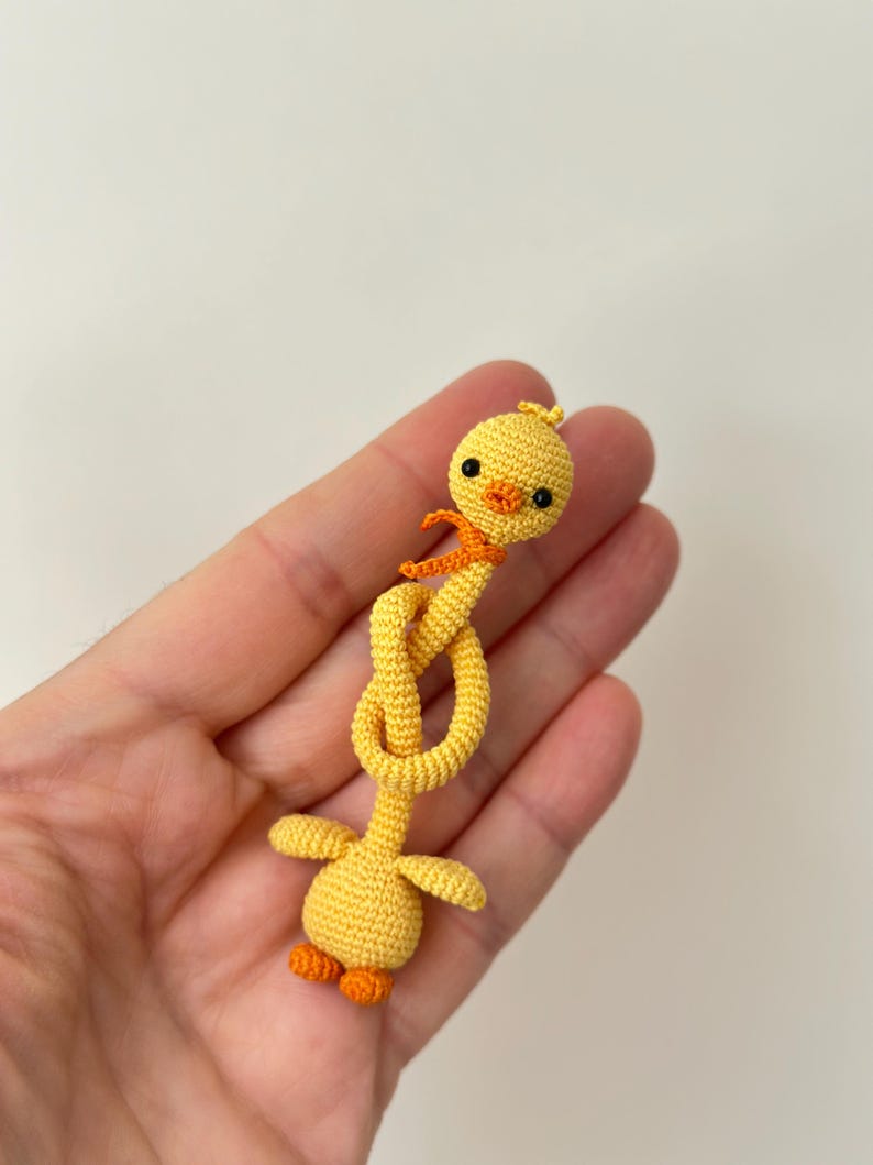 May include: A handmade yellow crochet duck with orange accents. The duck has a knotted neck, small wings, and orange feet. It is a whimsical, handcrafted item, perfect for a child's toy or a decorative piece.