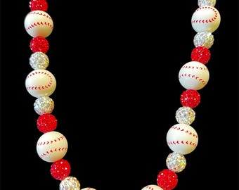 May include: A necklace with a baseball theme, featuring white baseball beads with red stitching, red faceted beads, and silver rhinestone beads. The necklace is set against a black backdrop.