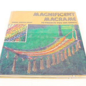 May include: A hardcover book titled Magnificent Macramé: 50 Projects You Can Create by Marie-Jeanine Solvit. The cover features a photograph of a colorful, multi-toned macramé hammock with long fringe tassels suspended between two trees in a grassy area.