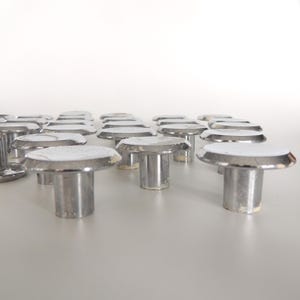 May include: A collection of silver-colored, mushroom-shaped cabinet knobs. Each knob has a flat, circular top with a white center and a cylindrical base. The knobs are arranged in rows against a white background, suggesting a hardware or home decor theme.