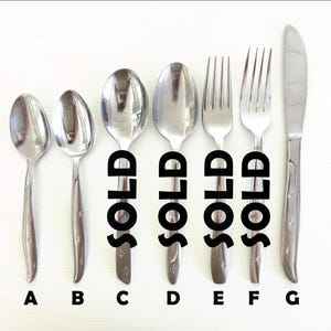 May include: A set of vintage silverware, including spoons, forks, and a knife, arranged on a white surface. The word "SOLD" is printed on some of the utensils. Each piece has a starburst design on the handle.