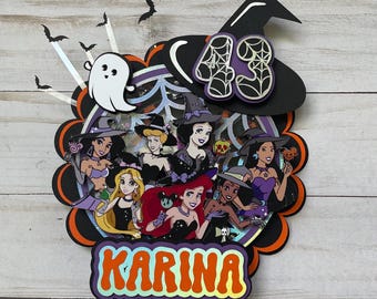May include: A Halloween cake topper with Disney princesses dressed as witches. The topper includes a witch's hat with the number 43, a ghost, bats, and the name "Karina" in orange and gold lettering. The design is layered with black, orange, and purple accents.