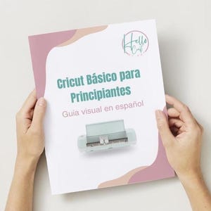 Puede incluir: Un papel blanco con el título "Cricut Básico para Principiantes" en color turquesa y el subtítulo "Guía visual en español". El papel tiene un diseño rosa claro y blanco y presenta una máquina Cricut turquesa. La imagen está sostenida por dos manos.