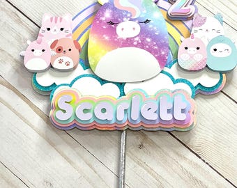 以下が含まれることがあります： 虹色のユニコーンのケーキトッパー。キラキラ光るパープルとピンクのユニコーン、虹、そして「Scarlett」という名前が虹色の文字で書かれています。トッパーには、数字の2と、小さな動物のキャラクターがいくつか付いています。