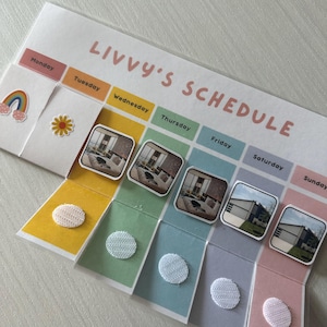 以下が含まれることがあります： 「Livvy's Schedule」というタイトルのカラフルな週間スケジュールプランナー。プランナーは週の曜日ごとに7つのセクションに分かれており、曜日ごとに異なる色が使われています。各セクションには、写真やその他のアイテムを入れるための小さな透明なポケットがあります。プランナーには、虹のステッカーと花のステッカーも付いています。