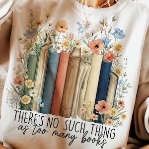 May include: Cream-colored sweatshirt featuring a floral and book design. The graphic includes colorful flowers and a row of books with the text "THERE'S NO SUCH THING as TOO MANY BOOKS". The top is from "DAVINCIPRINTSHOP" and is an "ORIGINAL DESIGNER" item.