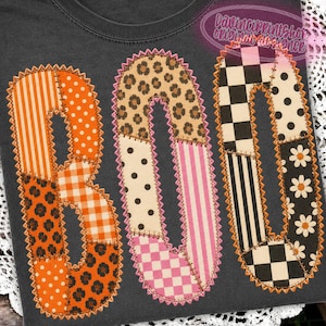 May include: A dark gray t-shirt featuring the word BOO in large, patchwork-style letters. Each letter is composed of various patterned segments including orange stripes, polka dots, leopard print, gingham, checkers, stripes, and white daisies.