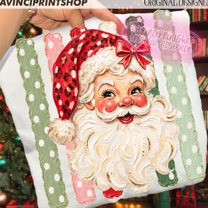 May include: A white sweatshirt featuring a painted Santa Claus with a red leopard print hat and a red bow. The design includes two vertical sage green stripes with white polka dots on either side of the Santa illustration, which has a textured finish.