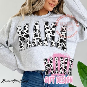 May include: A grey sweatshirt with a black and white cow print design that says "Mama Mini" in large, bold letters. The design is a distressed, vintage-style graphic. The sweatshirt is a popular gift design.
