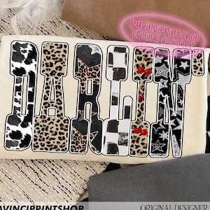 May include: A cream-colored graphic featuring the word "DARLIN" in a bold, stylized font. Each letter is filled with a unique pattern, including cow print, leopard print, stars, and cherries. The text "DAVINCIPRINTSHOP" and "ORIGINAL DESIGNER" are also visible.
