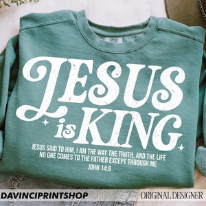 K&ouml;nnte beinhalten: Ein t&uuml;rkisfarbenes Sweatshirt mit einer wei&szlig;en Grafik, auf der in einer Retro-Schrift "JESUS is KING" steht. Die Grafik enth&auml;lt auch einen Bibelvers: "Jesus sagte zu ihm: Ich bin der Weg, die Wahrheit und das Leben. Niemand kommt zum Vater au&szlig;er durch mich. Johannes 14:6"