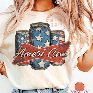 May include: A white t-shirt with a vintage-style graphic of three red, white, and blue cans with stars. The graphic says "Ameri Can" with a red ribbon and stars. The text "Davinciprintshop Original Designer" is in a circle above the cans.