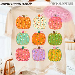Puede incluir: Una camiseta de color crema con una cuadr&iacute;cula de nueve calabazas ilustradas en varios colores, incluyendo naranja, turquesa, rosa, verde y morado. Cada calabaza est&aacute; decorada con un patr&oacute;n de lunares. El texto DAVINCIPRINTSHOP aparece arriba.