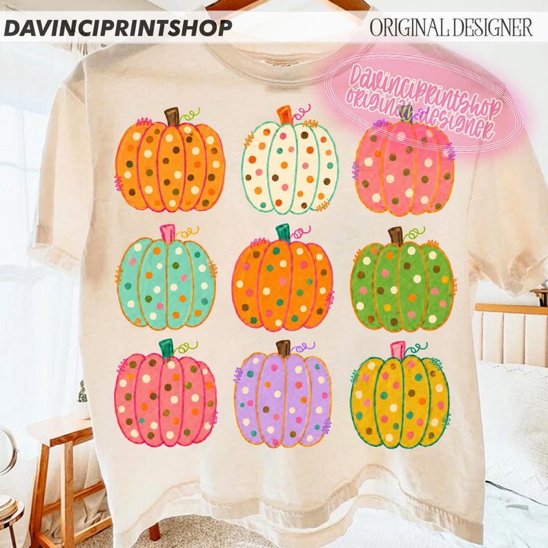 Puede incluir: Una camiseta de color crema con una cuadr&iacute;cula de nueve calabazas ilustradas en varios colores, incluyendo naranja, turquesa, rosa, verde y morado. Cada calabaza est&aacute; decorada con un patr&oacute;n de lunares. El texto DAVINCIPRINTSHOP aparece arriba.
