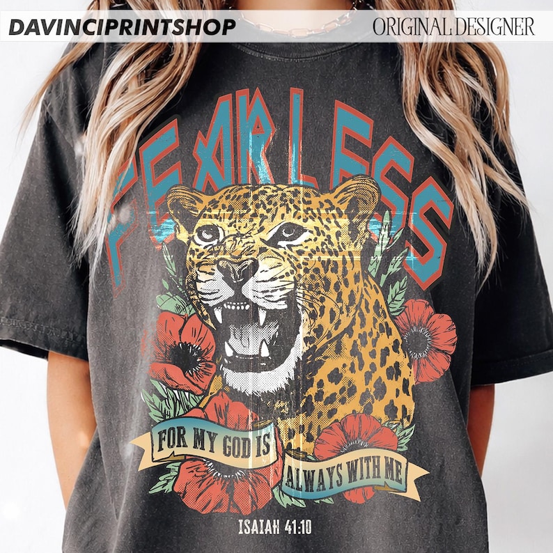 Puede incluir: Camiseta gris oscuro con un leopardo rugiente y la palabra "FEARLESS" en letras turquesas y rojas. El dise&ntilde;o incluye amapolas rojas y el texto "FOR MY GOD IS ALWAYS WITH ME" en una pancarta, con "ISAIAH 41:10" debajo.