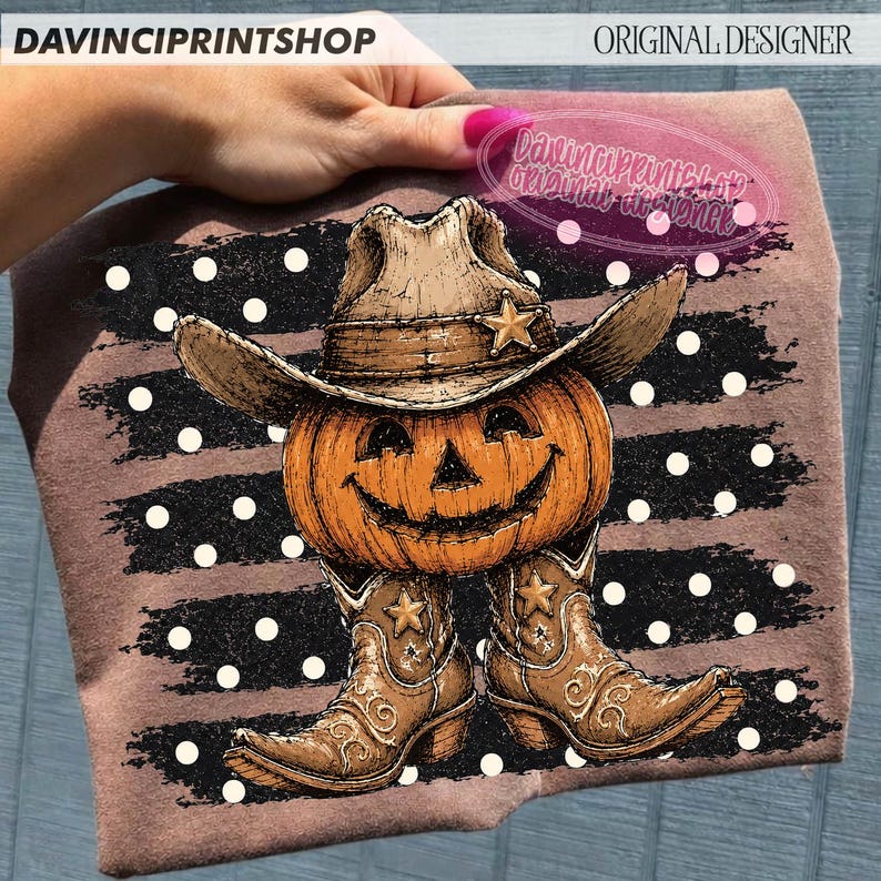 K&ouml;nnte beinhalten: Ein braunes T-Shirt mit einer Grafik eines orangefarbenen K&uuml;rbisses, der einen beigen Cowboyhut und braune Cowboystiefel tr&auml;gt. Das Motiv ist vor einem Hintergrund aus schwarzen horizontalen Pinselstrichen mit wei&szlig;en Punkten platziert.