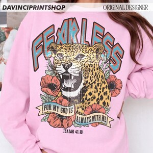 Puede incluir: Sudadera rosa claro con un leopardo rugiente, la palabra "FEARLESS" en verde azulado y naranja, y el texto "FOR MY GOD IS ALWAYS WITH ME" con el vers&iacute;culo b&iacute;blico Isa&iacute;as 41:10. El dise&ntilde;o incluye flores rojas.