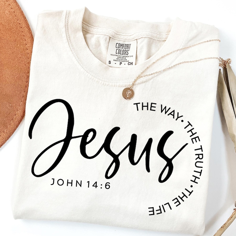 May include: A beige t-shirt with black text that reads "Jesus" and "John 14:6". The text is in a circle with the words "The Way, The Truth, The Life" around the outside.
