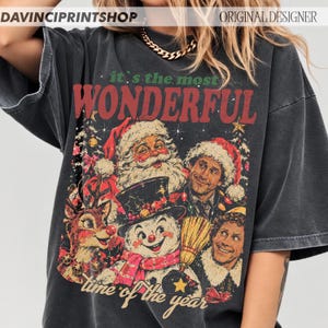 K&ouml;nnte beinhalten: Ein anthrazitfarbenes Oversize-T-Shirt mit einem Grafikdruck und dem Text "it's the most WONDERFUL time of the year". Das Design zeigt Illustrationen vom Weihnachtsmann, einem Rentier, einem Schneemann und zwei M&auml;nnern mit Weihnachtsm&uuml;tzen.