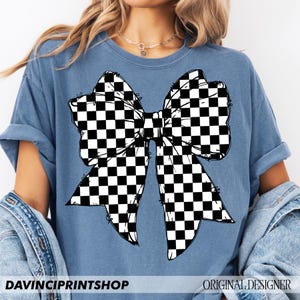 May include: A blue t-shirt featuring a large black and white checkered bow graphic. The shirt has short sleeves and a relaxed fit. The text "DAVINCIPRINTSHOP" is printed at the bottom left, and "ORIGINAL DESIGNER" is at the bottom right.