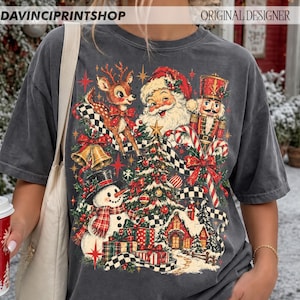 May include: A charcoal gray t-shirt featuring a vintage-style Christmas graphic. The design includes Santa Claus, a reindeer, a nutcracker, a snowman, a decorated tree, presents, and a house, all accented with red, green, and gold colors.