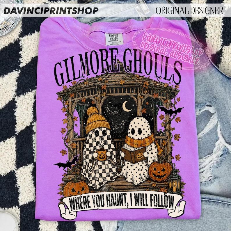 Puede incluir: Una camiseta de color morado claro con un gr&aacute;fico de dos fantasmas en un cenador. Un fantasma lleva un gorro y sostiene una taza, mientras el otro lee un libro. El dise&ntilde;o incluye calabazas, murci&eacute;lagos y el texto "GILMORE GHOULS" y "WHERE YOU HAUNT, I WILL FOLLOW."