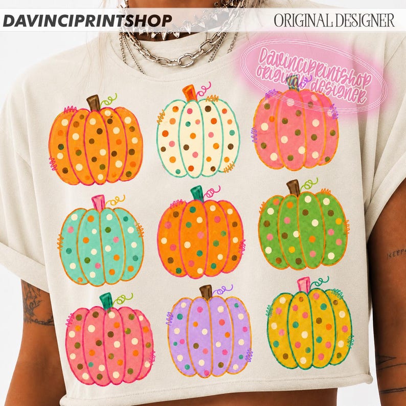 Puede incluir: Una camiseta de color crema con un estampado gr&aacute;fico de nueve calabazas dispuestas en cuadr&iacute;cula. Cada calabaza es de un color diferente, incluyendo naranja, blanco, rosa, turquesa, verde y morado, decoradas con lunares de colores.