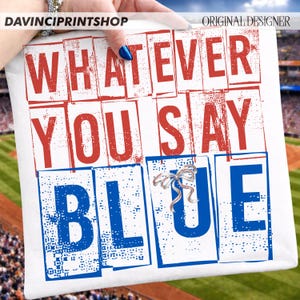 以下が含まれることがあります： 「WHATEVER YOU SAY BLUE」の文字が赤と青のブロック体でプリントされた白いクッション。銀色のリボンブローチが付いています。背景には野球場とスタジアムの座席が写っています。