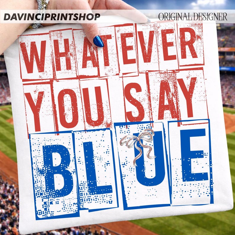 以下が含まれることがあります： 「WHATEVER YOU SAY BLUE」の文字が赤と青のブロック体でプリントされた白いクッション。銀色のリボンブローチが付いています。背景には野球場とスタジアムの座席が写っています。