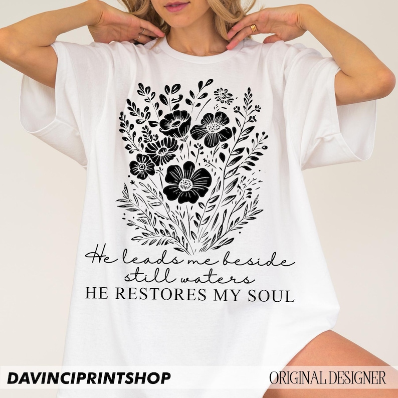 May include: White t-shirt with a black floral design and the text "He leads me beside still waters HE RESTORES MY SOUL".