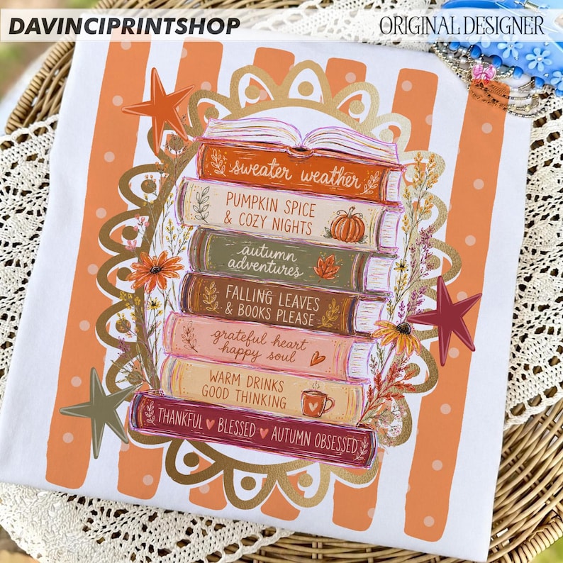 K&ouml;nnte beinhalten: Ein wei&szlig;es T-Shirt mit einem Stapel aus sechs B&uuml;chern mit orangefarbenen, gr&uuml;nen, braunen und rosafarbenen Buchr&uuml;cken. Die Buchtitel lauten: sweater weather, PUMPKIN SPICE & COZY NIGHTS, autumn adventures, FALLING LEAVES & BOOKS PLEASE, grateful heart happy soul, WARM DRINKS GOOD THINKING und THANKFUL BLESSED AUTUMN OBSESSED.