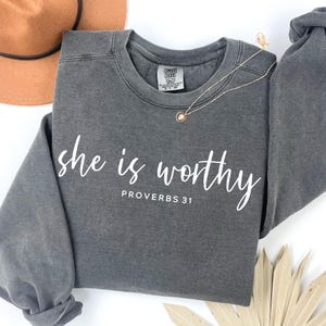 May include: Gray sweatshirt with the text "She is worthy Proverbs 31" in white.