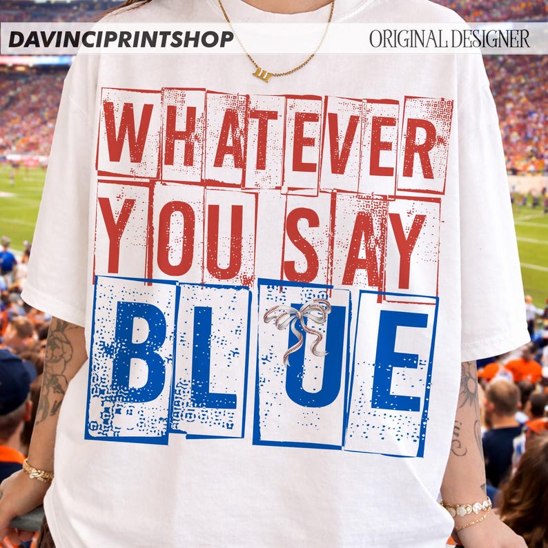 以下が含まれることがあります： 赤と青のブロック文字で「WHATEVER YOU SAY BLUE」と書かれた白いTシャツ。Tシャツはクルーネックと半袖です。テキストは、ヴィンテージスタイルです。