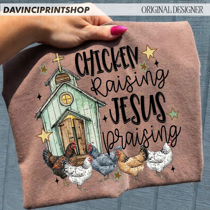 Peut inclure: Un t-shirt marron avec un motif d'&eacute;glise, de poulets et les mots "Chicken Raising Jesus Praising". Le motif comprend des &eacute;toiles et une croix. Le t-shirt est tenu par une main.