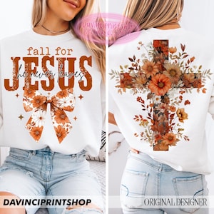 Op de afbeelding: Witte sweatshirt met de tekst "fall for JESUS he never leaves" in bruine letters. Een bloemenstrikontwerp staat onder de tekst. De achterkant van de sweatshirt heeft een kruisontwerp gevuld met oranje en bruine bloemen.