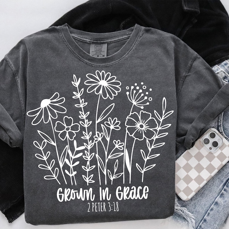Pode incluir: Uma camiseta cinza-chumbo com um gr&aacute;fico branco de flores e o texto "Grown in Grace 2 Peter 3:18".