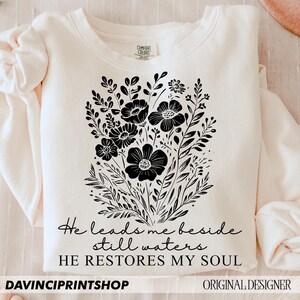 May include: A cream-colored sweatshirt with black floral design and the text "He leads me beside still waters HE RESTORES MY SOUL".