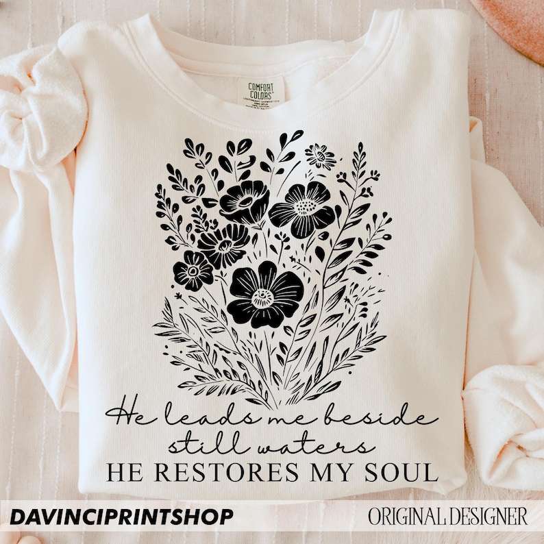 May include: A cream-colored sweatshirt with black floral design and the text "He leads me beside still waters HE RESTORES MY SOUL".