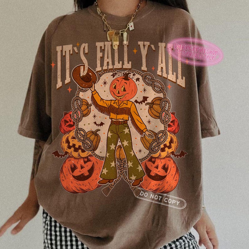 May include: Brown t-shirt with the text "IT'S FALL Y'ALL" in a vintage style. The graphic features a pumpkin-headed cowboy surrounded by pumpkins and rope. The cowboy is wearing a hat, fringe jacket, and star-patterned pants.