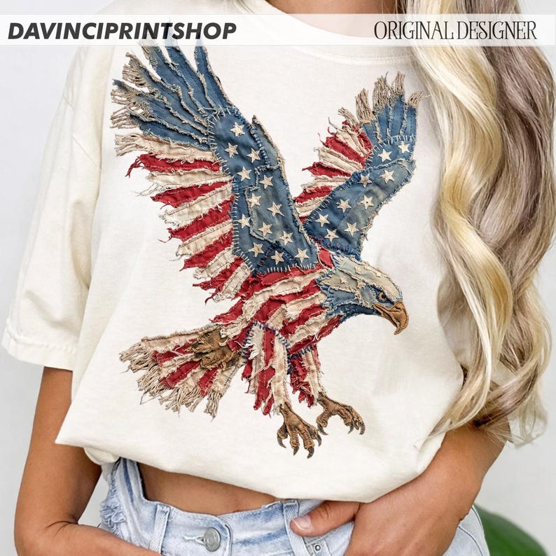 Pu&ograve; includere: T-shirt color crema con un design di aquila della bandiera americana invecchiata. Le ali dell'aquila sono spiegate, mostrando strisce rosse e bianche e toppe blu con stelle bianche. I testi "DAVINCIPRINTSHOP" e "ORIGINAL DESIGNER" sono visibili.