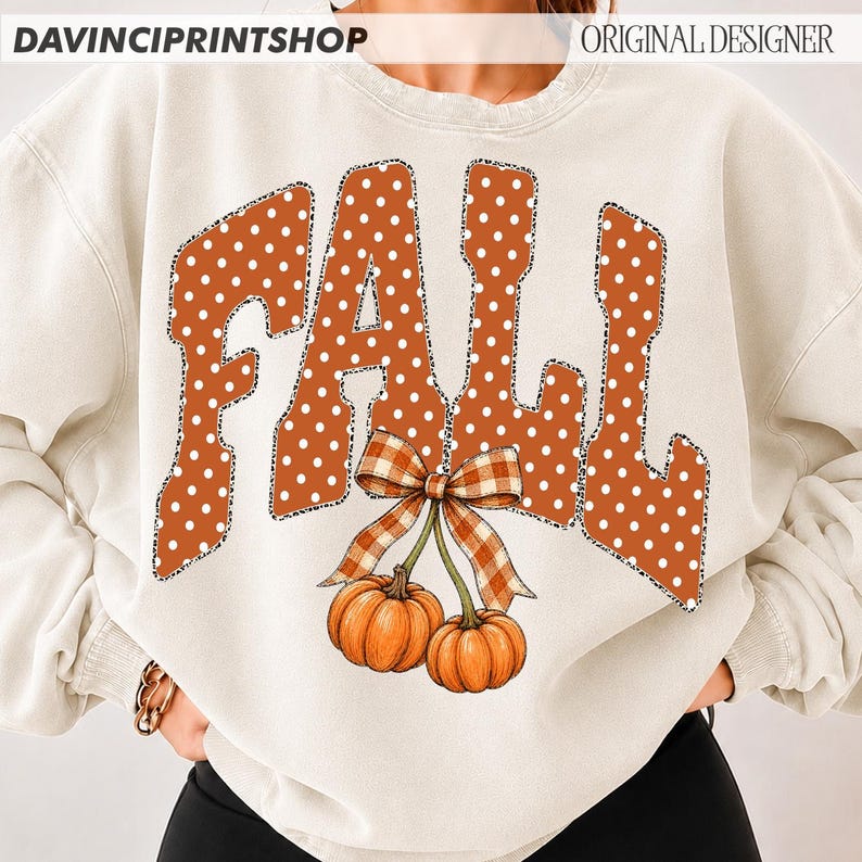 May include: A cream-colored crewneck sweatshirt featuring the word FALL in large, orange, white-polka-dotted letters with a leopard print outline. Below the text, two orange pumpkins are tied together with a brown and white checkered bow.