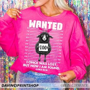 Puede incluir: Sudadera rosa con una ilustraci&oacute;n de oveja negra y el texto "WANTED" y "I once was lost, but now I am found. -LUKE 15:10".