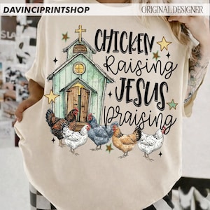 Peut inclure: T-shirt cr&egrave;me avec un motif fantaisiste. Le graphisme comprend une &eacute;glise, des poulets, des &eacute;toiles et les mots "Chicken Raising Jesus Praising". Le design est dans les tons de vert, marron et noir.