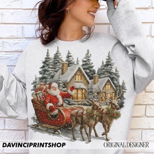 May include: A light grey sweatshirt with a festive Christmas design. It depicts Santa Claus in a red sleigh, reindeer, snow-covered houses, and fir trees. The text "DAVINCIPRINTSHOP" and "ORIGINAL DESIGNER" are visible at the bottom.
