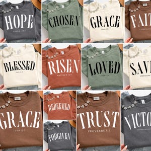 K&ouml;nnte beinhalten: Eine Sammlung von Sweatshirts mit Rundhalsausschnitt in verschiedenen Farben, die jeweils ein anderes religi&ouml;ses Wort in fetter wei&szlig;er Schrift tragen. Die W&ouml;rter sind "HOPE", "CHOSEN", "GRACE", "FAITH", "BLESSED", "RISEN", "LOVED", "SAVED", "TRUST", "VICTORY" und "FORGIVEN".